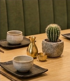 Handmade ceramic bowls, a brass carafe, and a potted cactus on a wood table at Fushion Café